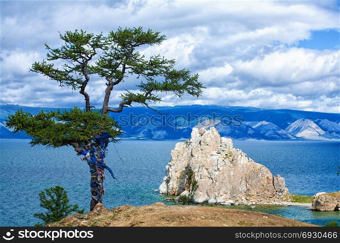 Beautiful View of the Sacred Siberian stone Shamanka at Cape Burhan, Olkhon Island on the island of Baikal, Siberia, Russia with Green Larch in Cloudy Summer Day