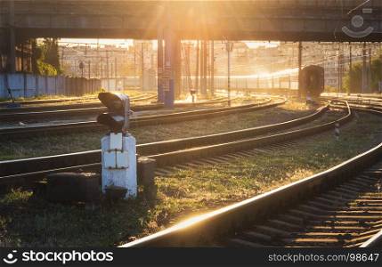 Beautiful view with traffic light, railroad and moving train at sunset. Railway station. Colorful industrial landscape with railway platform, semaphore, train and yellow sunlight. Railway background