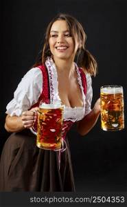 Beautiful waitress wearing traditional dirndl and holding two mass beer steins over black background.