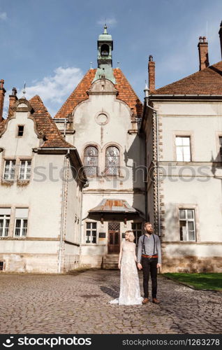 Beautiful wedding couple are walking near old castle, ancient restored architecture, old building, old house outside, vintage palace outdoor. Romantic love in vintage atmosphere street.. Beautiful wedding couple are walking near old castle, ancient restored architecture, old building, old house outside, vintage palace outdoor. Romantic love in vintage atmosphere street