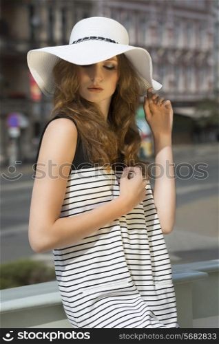 Beautiful, well dressed woman in summer hat on the street in sunny day. She has got brown, curly, long hair and nice make up.