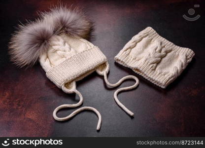 Beautiful white knitted winter cap with pompons on a dark concrete background. Clothes for winter cold. Beautiful white knitted winter cap with pompons on a dark concrete background