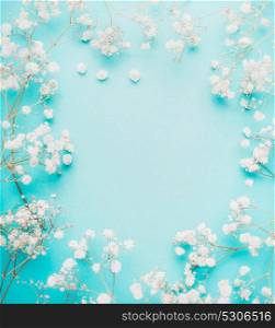 Beautiful white little flowers on light blue turquoise background, top view, frame.