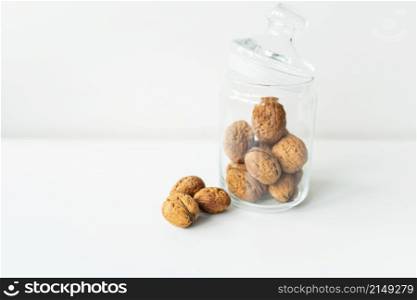 Beautiful whole walnut kernels in a glass jar, whole nuts in the shell can be seen nearby, on a white table. The concept of proper storage of walnuts. Selective focus. Beautiful whole walnut kernels in a glass jar, whole nuts in the shell can be seen nearby, on a white table. The concept of proper storage of walnuts. Selective focus.