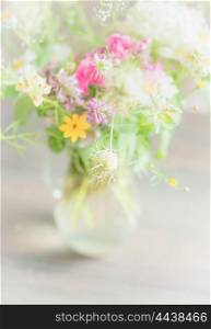 Beautiful wild flowers bunch in glass vase on light background, soft focus, close up. Home decoration and interior