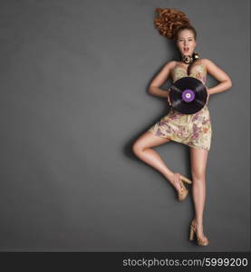 Beautiful winking girl, wearing vintage music headphones around his neck and holding an old vintage photo camera with bulb flash on chalkboard background.