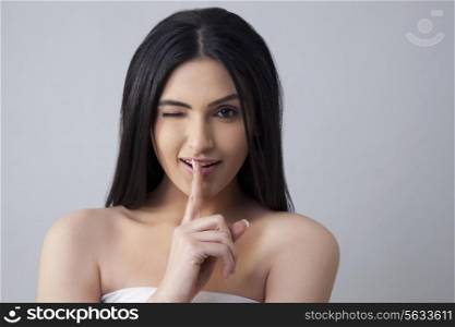 Beautiful winking woman gestures for silence over colored background