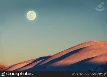 Beautiful winter landscape, amazing view on the moon by day over mountains covered with snow, stunning wintertime nature
