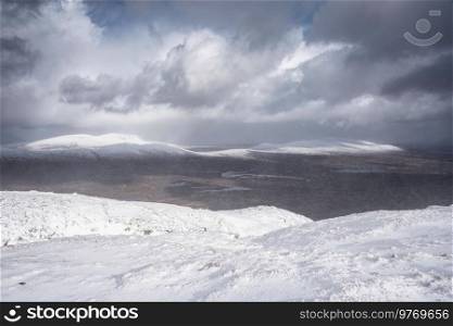 Beautiful Winter landscape image from mountain top in Scottish Highlands down towards Rannoch Moor during snow storm and spindrift off mountain top in high winds