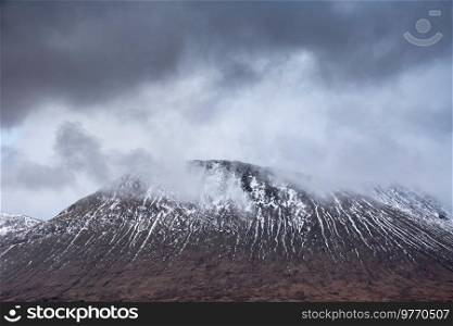 Beautiful Winter landscape image of Beinn A’ Chaladair in Scotland with dramatic skies overhead