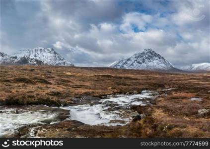 Beautiful Winter landscape image of River Etive in foreground with iconic snowcapped Stob Dearg Buachaille Etive Mor mountain in the background