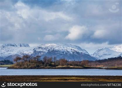 Beautiful Winter landscape view along Loch Leven past Ballachulish Bridge towards snowcapped mountains in distance with dramatic sky