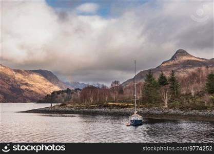 Beautiful Winter landscape view along Loch Leven towards snowcapped mountains in distance with moored sailing yacht in the foreground