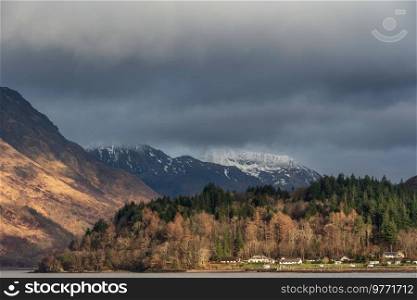 Beautiful Winter landscape view along Loch Leven towards snowcapped mountains in distance with dramatic sky