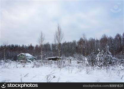 Beautiful winter landscape with abandoned old wooden buildings on a frosty cloudy day.