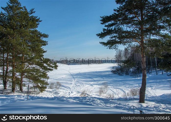 Beautiful winter landscape with snow-covered river and pine trees on a Sunny day.