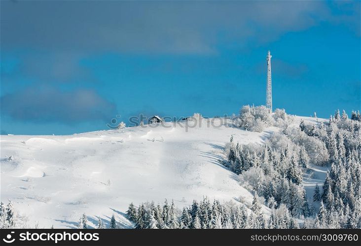 Beautiful winter rime frosting trees, communication tower and snowdrifts on mountain top on blue cloudy sky background (Carpathian mountain, Ukraine). People are unrecognizable.