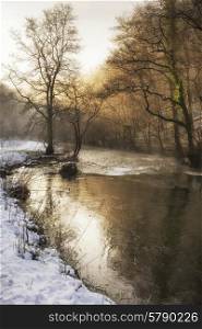 Beautiful Winter snow covered countryside landscape of river flowing with reflections