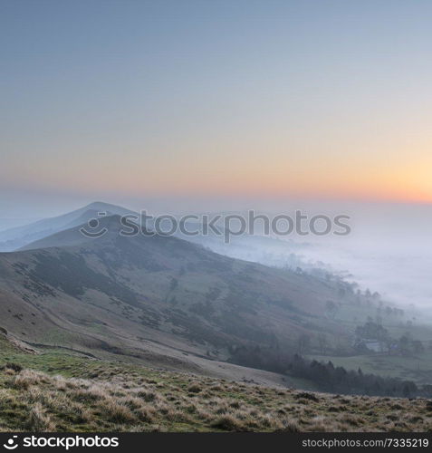 Beautiful Winter sunrise landscape image of The Great Ridge in the Peak District in England with a cloud inversion and mist in the Hope Valley with a lovely orange glow