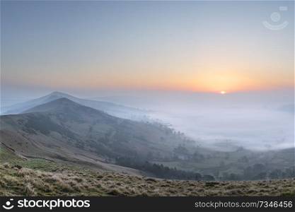 Beautiful Winter sunrise landscape image of The Great Ridge in the Peak District in England with a cloud inversion and mist in the Hope Valley with a lovely orange glow