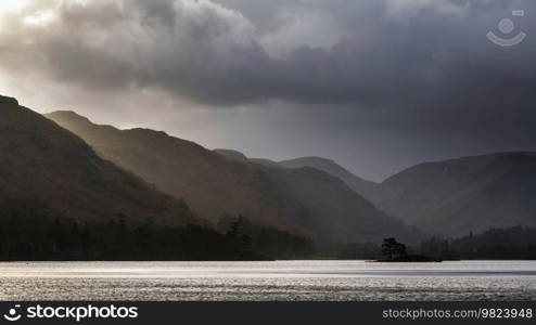 Beautiful Winter sunrise landscape over Ullwater in English Lake District with mist over lake giving a moody dramatic feel