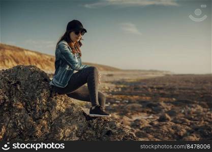 Beautiful woman alone in the beach sitting on the rocks