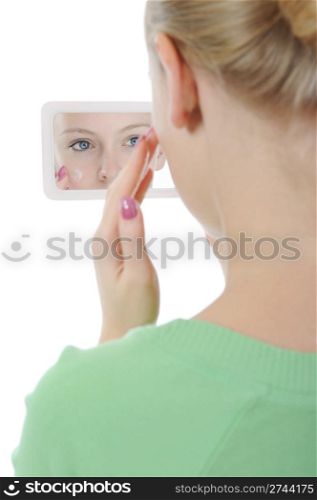 beautiful woman applying cream on her cheek front of the mirror. Isolated on white background