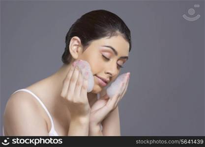 Beautiful woman applying soap sud on face against gray background