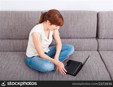 Beautiful woman at home lying on sofa and working with a laptop