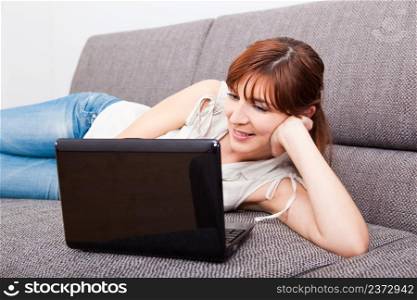 Beautiful woman at home lying on sofa and working with a laptop