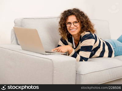 Beautiful woman at home lying on the sofa and working with a laptop