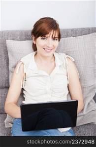 Beautiful woman at home seated on sofa and working with a laptop