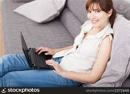 Beautiful woman at home seated on sofa and working with a laptop