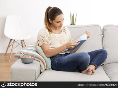 Beautiful woman at home sitting on the couch and reading a book