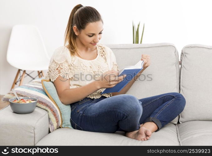 Beautiful woman at home sitting on the couch and reading a book