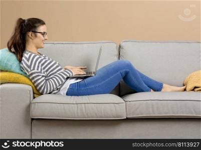 Beautiful woman at home sitting on the sofa and working with a laptop