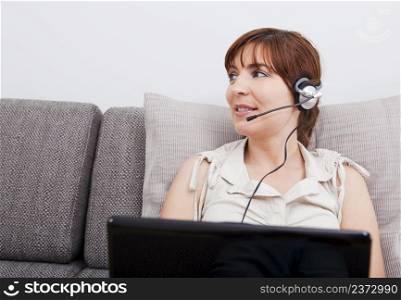 Beautiful woman at home with a laptop, and speaking over the internet with headphones
