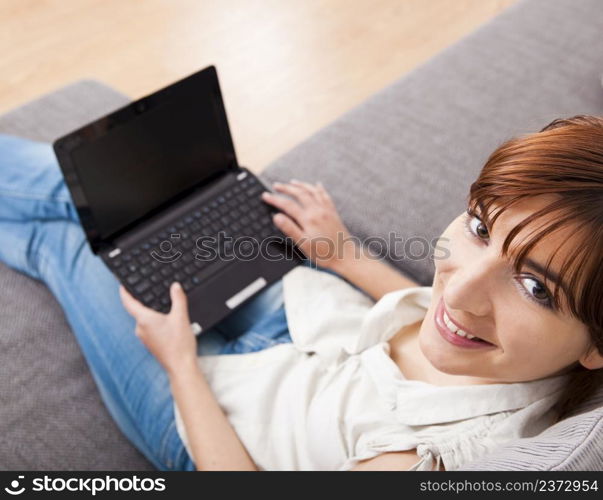 Beautiful woman at seated on sofa and working with a laptop