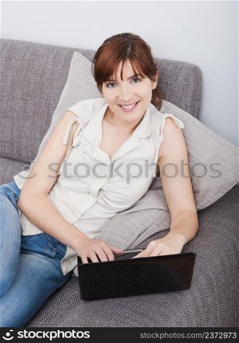 Beautiful woman at seated on sofa and working with a laptop