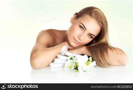 Beautiful woman at spa, pretty girl lying down on massage table with gentle white orchid flowers, wellbeing and healthy lifestyle concept