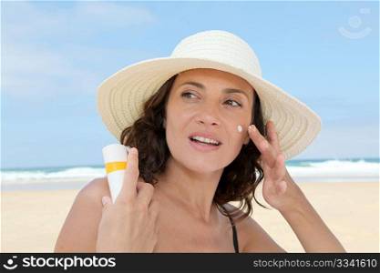 Beautiful woman at the beach putting sunscreen on her body