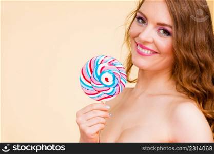 Beautiful woman bare shoulders holding big lollipop candy in hand, closeup. Sweet food and fun concept. Studio shot on bright. Woman holds colorful lollipop candy in hand