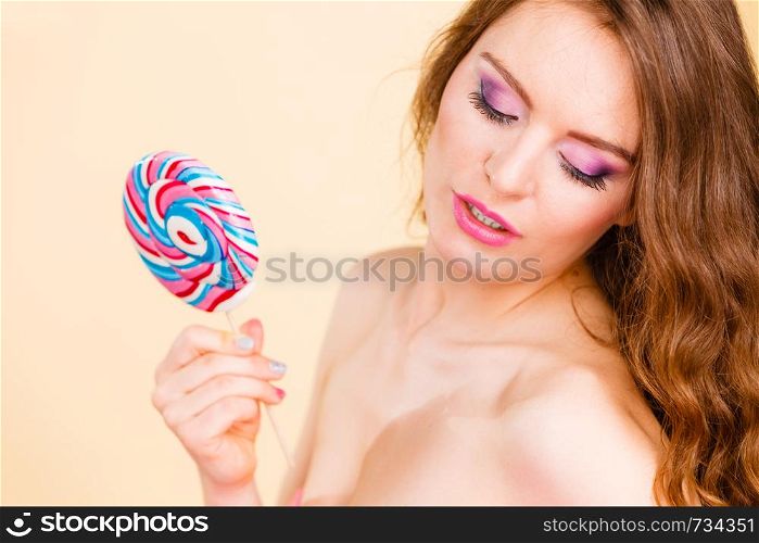 Beautiful woman bare shoulders holding big lollipop candy in hand, closeup. Sweet food and fun concept. Studio shot on bright. Woman holds colorful lollipop candy in hand