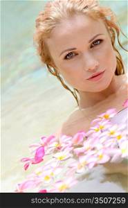 Beautiful woman bathing in pool with frangipani flowers