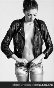 Beautiful woman body in denim jeans shorts and black leather jacket. Black and white studio shot.