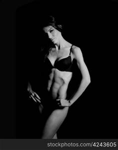 beautiful woman bodybuilder posing in black bikini on black background