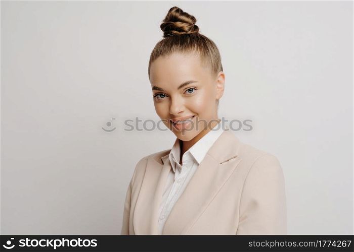 Beautiful woman business manager in classic wear looking forward with charming smile and confident assertive look in her eyes while standing next to light background. Successful business people. Beautiful business woman with confident look in eyes