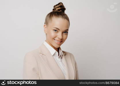 Beautiful woman business manager in classic wear looking forward with charming smile and confident assertive look in her eyes while standing next to light background. Successful business people. Beautiful business woman with confident look in eyes