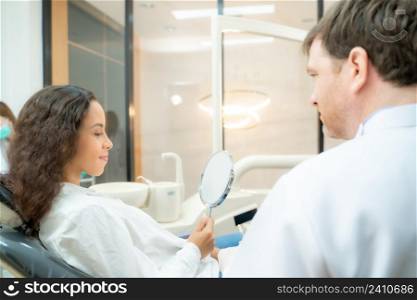 Beautiful woman checking teeth after curing teeth in dental clinic,Woman looking at mirror with smile.