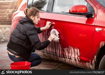 Beautiful woman cleaning car door from mud and dirt